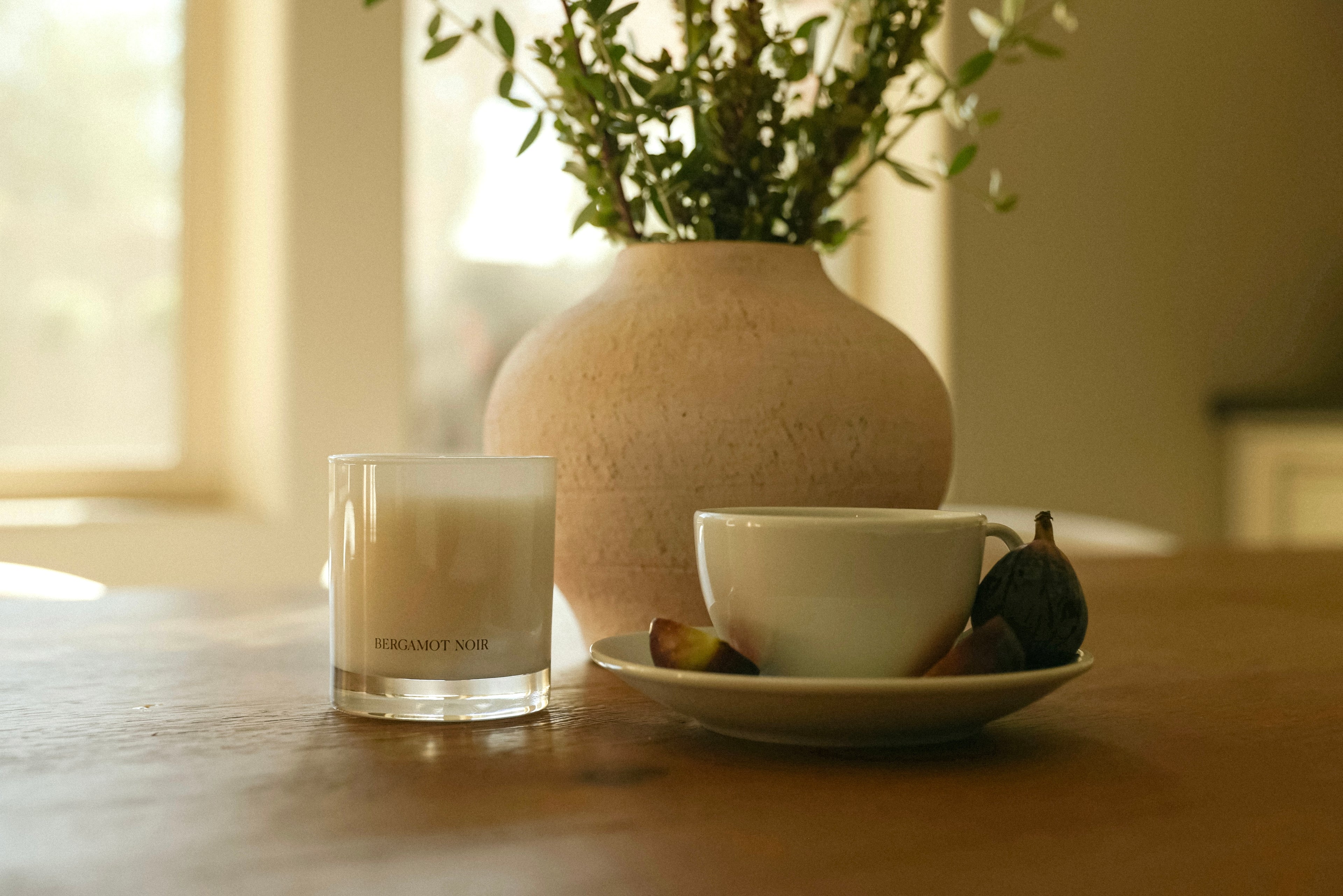 CHENDA STUDIO No. 03 Bergamot Noir candle styled beside a ceramic cup, figs and greenery